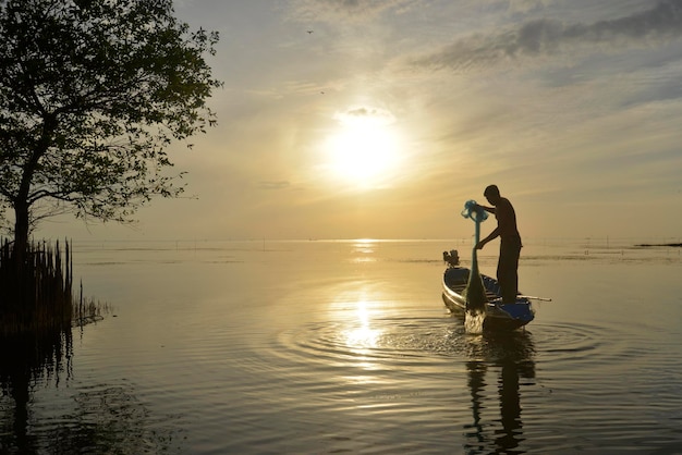 Ein Fischer reinigt ein Fischernetz mit Sonnenaufgang im Hintergrund