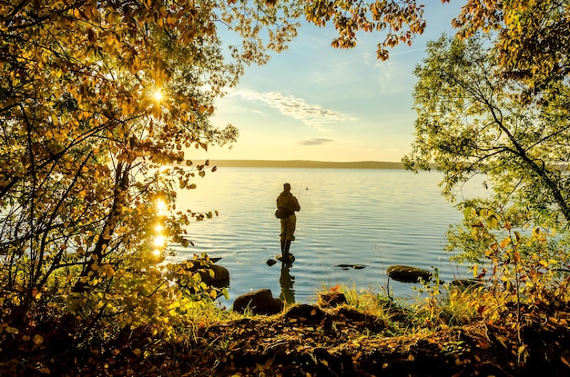 Ein Fischer steht an einem Herbstmorgen auf einem Felsen im See.