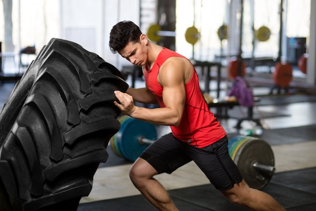 Ein fitter, athletischer junger Mann in der Sportbekleidung, die Kraftübung mit großem Rad im Fitnessstudio macht.