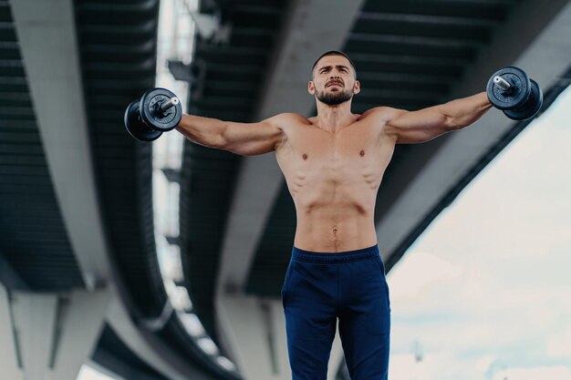 Foto ein fitter, bärtiger mann hebt unter einer brücke gewichte und demonstriert damit seine entschlossenheit als kraftvoller bodybuilder