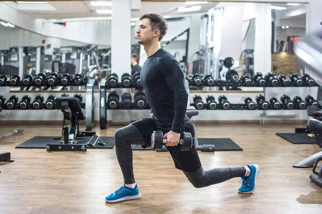Ein fitter, hübscher junger Mann trainiert mit Gewichten im Fitnessstudio