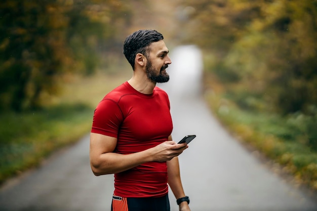 Foto ein fitter läufer steht auf einer straße in der natur und benutzt eine fitness-anwendung auf seinem handy