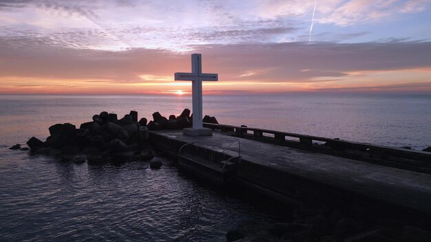 Ein Flug um ein christliches Kreuz am frühen Morgen bei Sonnenaufgang Das große Kreuz steht am Rande eines Wellenbrechers an der Meeresküste