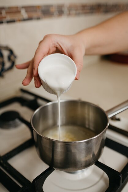 Ein Foto einer Hand einer Frau, die Sahne aus der Tasse in den Topf mit Zitronensaft und Zitronenschale auf dem Gasherd gießt