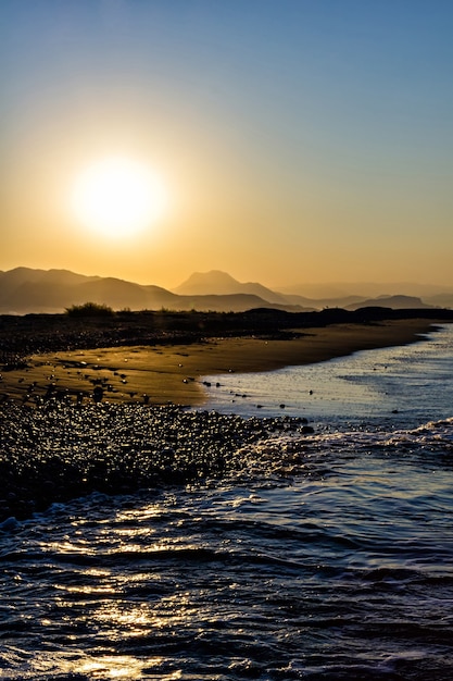 Ein Foto von einem Strand und einem Berg bei Sonnenaufgang