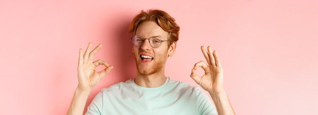 Foto ein frecher rothaariger typ mit brille, der dir mit einem augenzwinkern versichert und okay-schilder zeigt, garantiert gutes personal