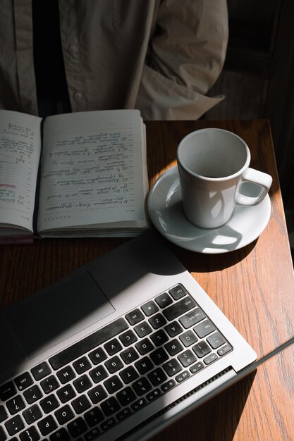 Ein freiberufliches Mädchen arbeitet in einem Café an einem Laptop, trinkt schwarzen Kaffee und macht sich Notizen in einem Notizbuch