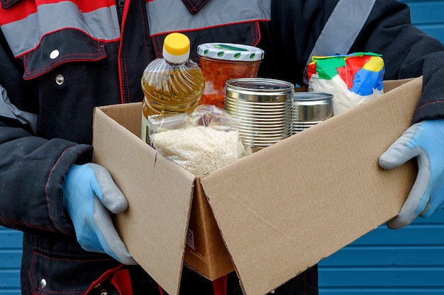 Ein Freiwilliger in einer Winterjacke hält einen Karton mit trockenem Getreide, Konserven, Butter und anderen Produkten.