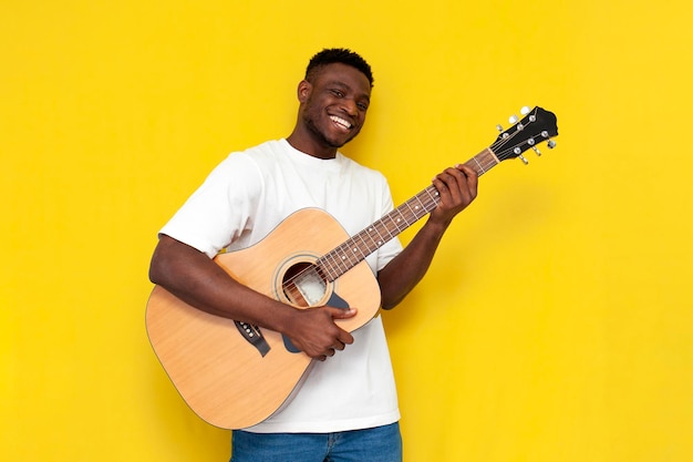 Ein freudiger afroamerikanischer Mann hält eine akustische Gitarre und singt auf einem gelben, isolierten Hintergrund