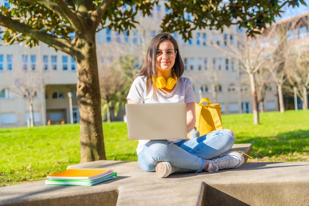 Ein freudiger Schüler sitzt vor dem Campus und benutzt einen Laptop