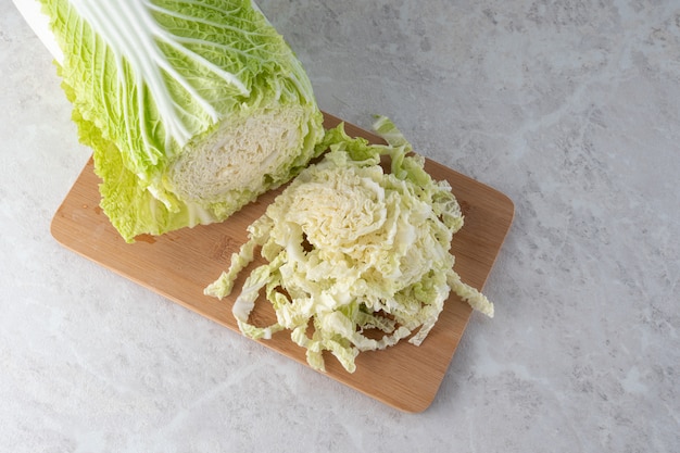 Ein frischer Pekinger Kohlkopf wird gehackt, um einen Salat zuzubereiten. Marmor Hintergrund.