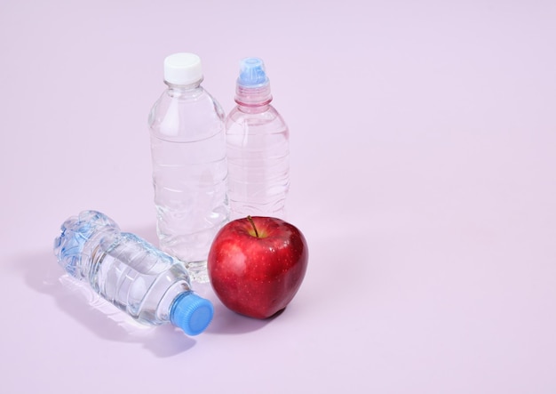 Ein frischer reifer roter Apfel und Flaschen mit sauberem Trinkwasser auf violettem Hintergrund. Die richtige Ernährung und eine gesunde Lebensweise. Kopierraum für Text