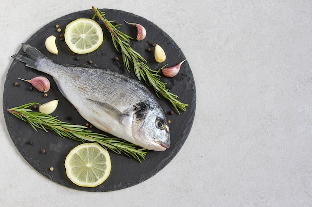 Ein frischer, roher Bio-Dorado oder Seebrasse mit Gewürzen und Zitrone auf grauem Hintergrund Kopierbereich