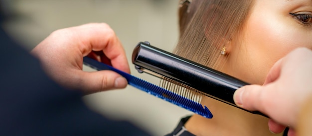 Ein Friseur glättet der jungen Brünetten in einem Schönheitssalon die Haare.