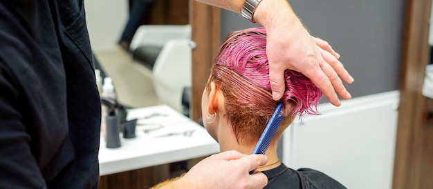 Ein Friseur kämmt die rosa gefärbten nassen kurzen Haare der Kundin in der Rückansicht des Friseursalons