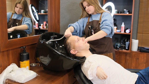Ein Friseurmädchen wäscht einem Mann mit eingeschränkten Möglichkeiten in einem Schönheitssalon die Haare