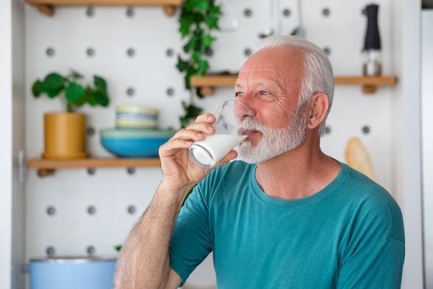 Ein fröhlicher älterer Mann nippt in einer gemütlichen Küche an frischer Milch aus einem Glas. Sein glückliches Gesicht strahlt Freude aus, während er den cremigen Genuss umgeben von warmem Sonnenlicht und einer heimeligen Atmosphäre genießt