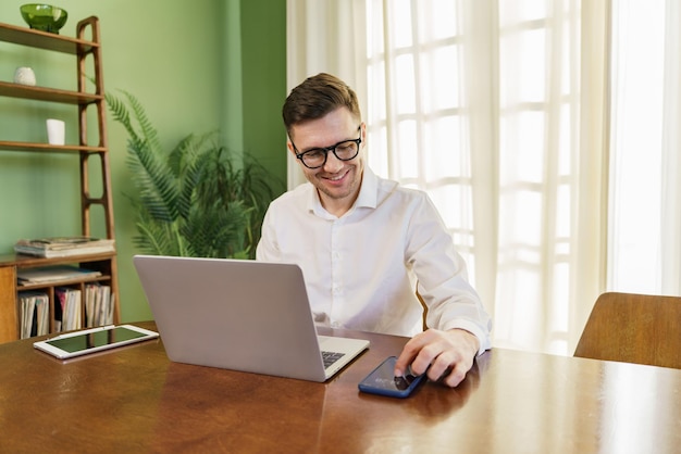 Ein fröhlicher Fachmann bedient gleichzeitig einen Laptop und ein Smartphone, umgeben von