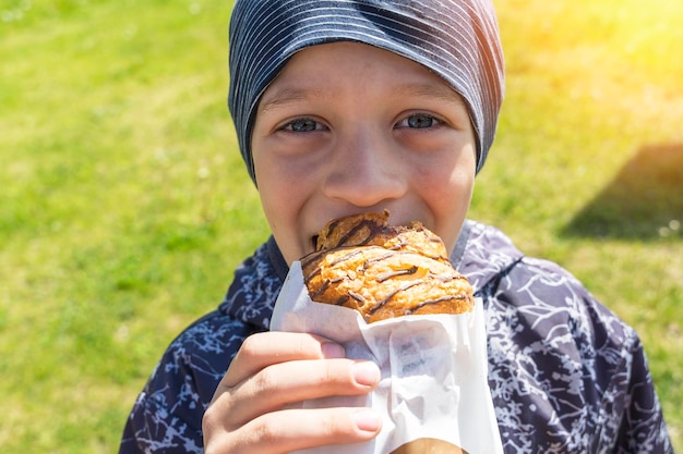 Ein fröhlicher fröhlicher Junge isst ein Brötchen auf der Straße