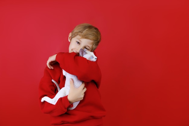 Ein fröhlicher Junge in einem roten Trainingsanzug umarmt ein kleines Kätzchen und streichelt ihn