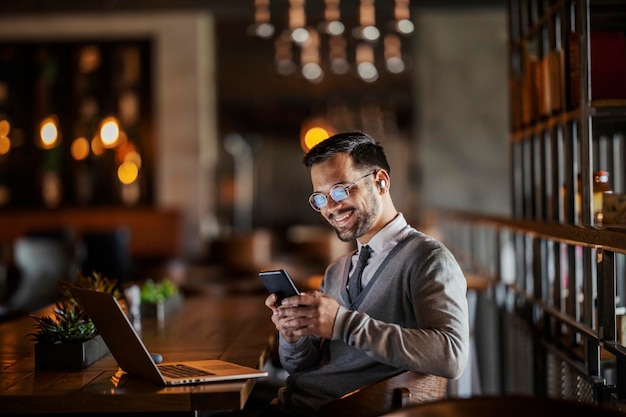 Ein fröhlicher junger Geschäftsmann sitzt mit seinem Laptop im Café