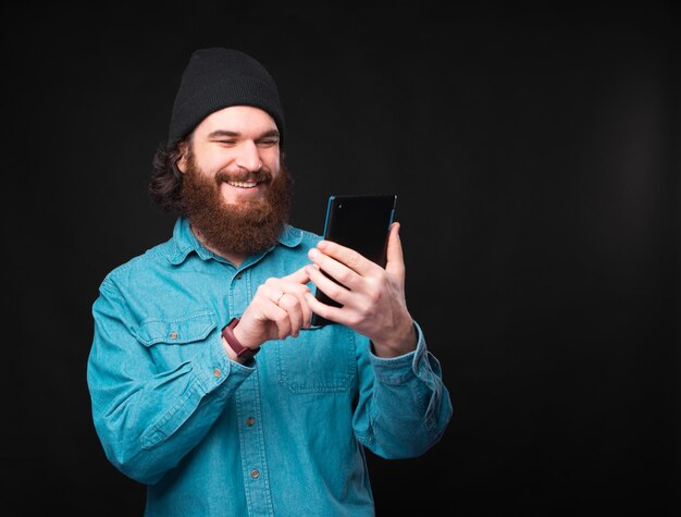 Ein fröhlicher junger Mann schreibt eine Nachricht auf sein brandneues Tablet in der Nähe einer dunklen Wand