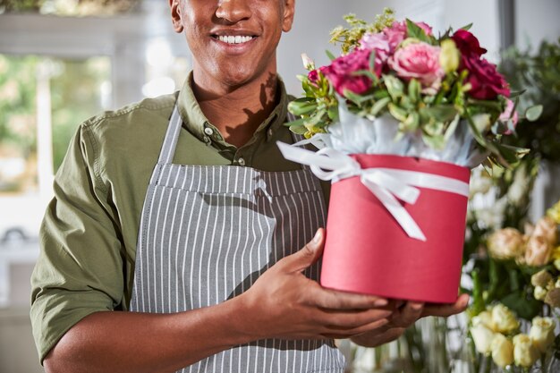 ein fröhlicher multiethnischer Florist, der ein schönes Blumenarrangement in einem Topf präsentiert