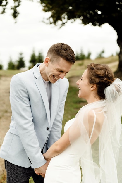 Ein fröhliches Hochzeitspaar geht am Hochzeitstag in den Bergen unter einem großen und schönen verzweigten Baum spazieren