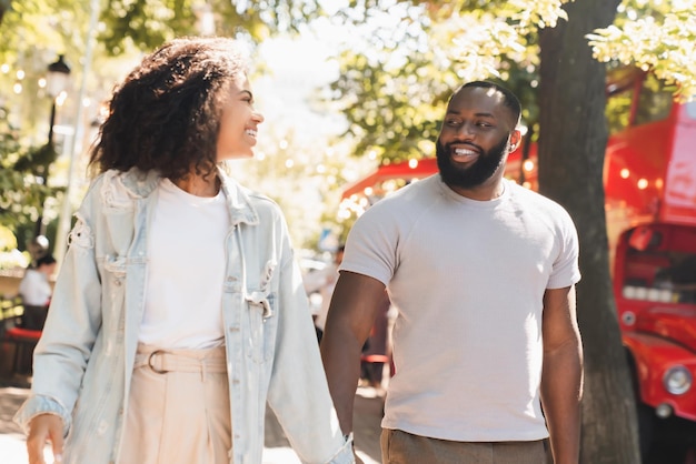 Ein fröhliches junges afrikanisches Paar geht zusammen auf einem romantischen Date im Freien im Stadtpark.