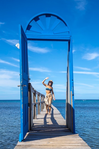 Ein fröhliches junges Mädchen an einer blauen Tür im Karibischen Meer auf der Insel Roatan, Honduras