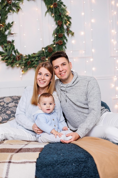 Ein fröhliches junges Paar mit einem kleinen Sohn spielt auf dem Bett in der Nähe des Weihnachtsbaums Neujahrs-Interieur im Schlafzimmer Weihnachtsbaum mit Spielzeug Festliche Familienatmosphäre