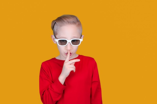 Ein fröhliches Kind mit 3D-Kinderbrille legt seinen Zeigefinger an die Lippen und macht eine leise Geste