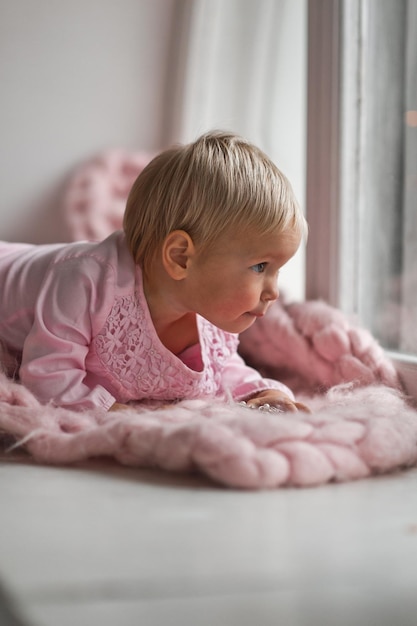 Ein fröhliches kleines Mädchen spielt auf der Fensterbank 2018