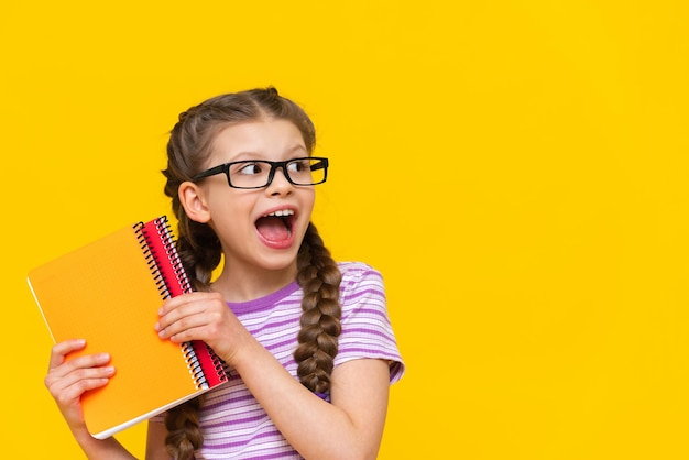 Ein fröhliches Mädchen mit Notebooks auf einem isolierten gelben Hintergrund Das Schulmädchen ist sehr glücklich