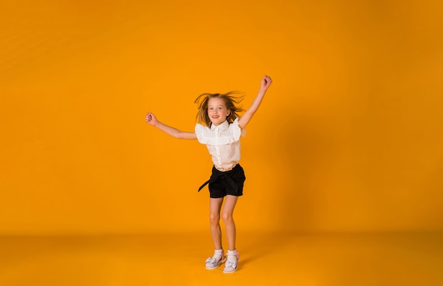 Ein fröhliches Schulmädchen in Uniform springt auf gelbem Hintergrund mit einer Kopie des Raumes