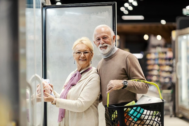 Ein fröhliches Seniorenpaar kauft Tiefkühlprodukte aus dem Kühlschrank im Supermarkt