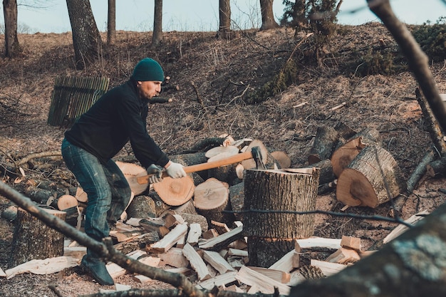 Ein frostiger Mann erntet Holz für den kalten Winter und schneidet eine dicke massive Esche