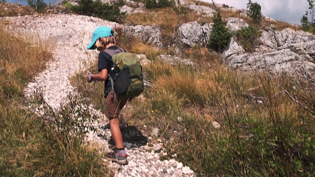 Ein fünfjähriger Junge mit Rucksack geht voller Aufregung einen sommerlichen Bergweg entlang und ist bereit, die Welt um ihn herum zu erkunden