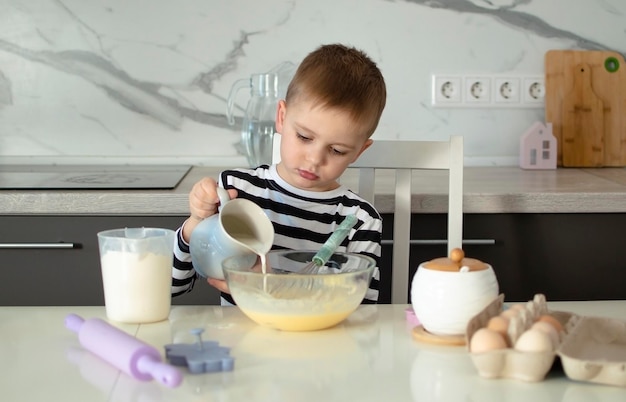 Foto ein fünfjähriger junge spielt in der küche mit teig. ein kind backt kekse. ein porträt eines fröhlich lächelnden kindes, das teig knetet. kinder lernen neue dinge.