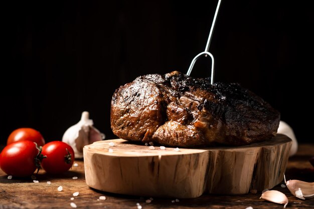 Ein gebackenes ganzes Stück Fleisch und rohes Gemüse auf einem Holzständer Ein Stück Schweine- oder Rindfleisch, das im Ofen mit Gewürzen gegart wird