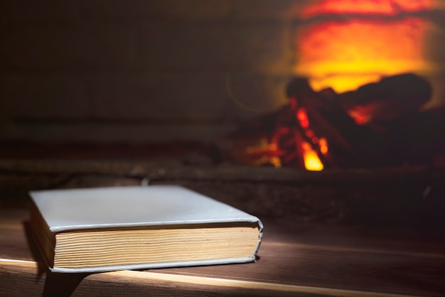 Ein gebundenes Buch liegt auf einem hölzernen nahe einem brennenden Kamin