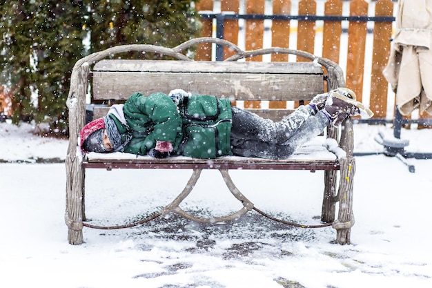 Ein gefrorenes Kind schläft allein auf einer Bank vor einem Schneehintergrund