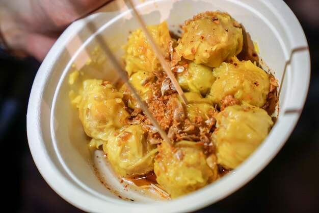 Ein gelber gedämpfter Knödel mit gebratenem Knoblauch in den Pappbecher gelegt In Bangkok Thailand Foodstruck Streetfood