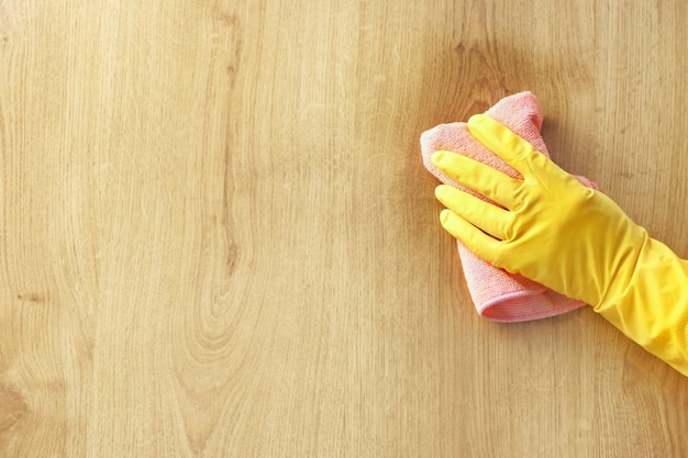 Ein gelber Gummihandschuh der weiblichen Hand wischt einen Schmutzfleck auf dem rosa Tuch des hölzernen Parkettbodens ab