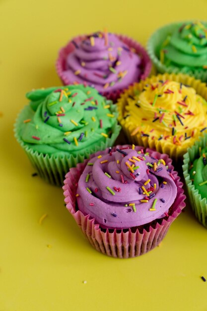 ein gelber Tisch mit lila und grünen Cupcakes mit lila Glasur und Sprinkles