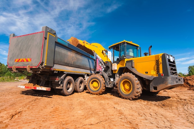 ein gelber Traktor lädt Erde in einen Muldenkipper