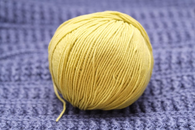 Ein gelbes Wollknäuel liegt auf einer blauen Wolltischdecke. Foto in hoher Qualität