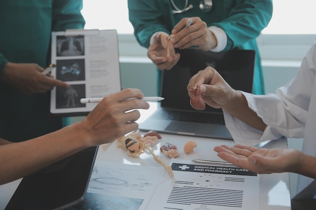 Ein gemischtrassiges medizinisches Team trifft sich mit Ärzten in weißen Laborkitteln und OP-Kitteln, die an einem Tisch sitzen und die Patientenakten besprechen