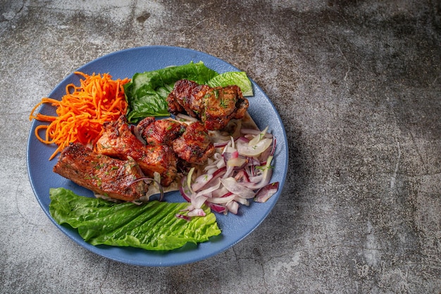 Ein Gericht aus der Speisekarte des Restaurants servieren. Gegrilltes Rind- und Schweinefleisch mit geriebenen Karotten und Kräutern auf einem Teller gegen einen grauen Steintisch, leckerer Kebab