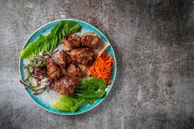 Ein Gericht aus der Speisekarte des Restaurants servieren. Gegrilltes Rind- und Schweinefleisch mit geriebenen Karotten und Kräutern auf einem Teller gegen einen grauen Steintisch, leckerer Kebab